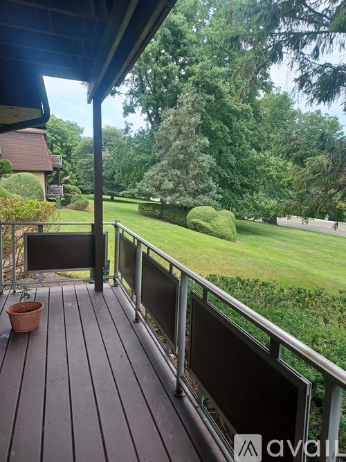 A balcony with a potted plant and a view of a green lawn and trees.