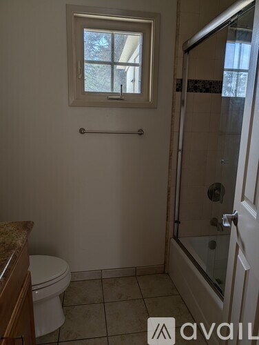 A bathroom with a toilet, a window, and a glass shower door.