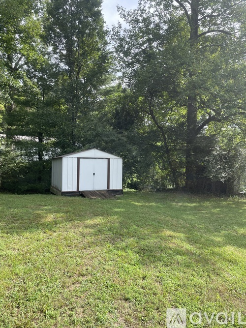 A small white shed sits in a grassy field with trees in the background.