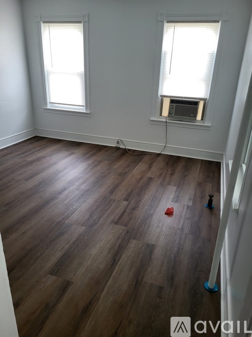 A room with wooden flooring and two windows.