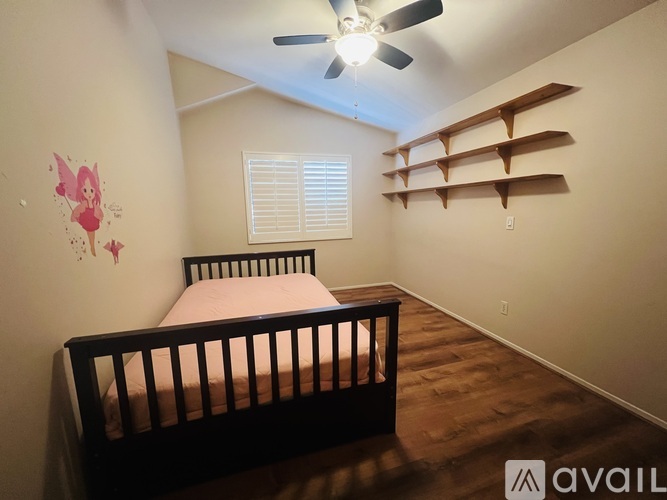 A bedroom with a bed, a ceiling fan, and a wall with a pink fairy decoration.