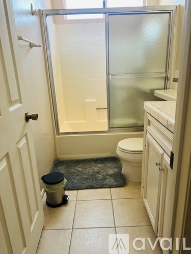 A bathroom with a toilet, a trash can, and a walk-in shower.