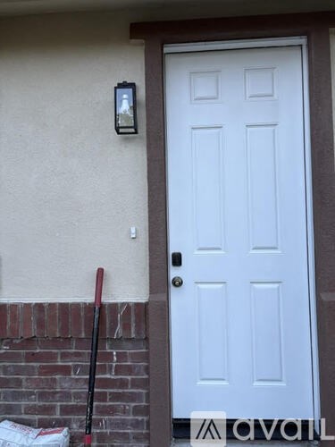 A white door with a black handle and a black stick leaning against a brick wall.