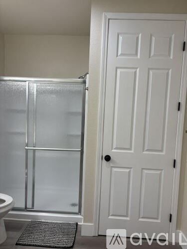 A white door with a black mat in front of a glass shower stall.
