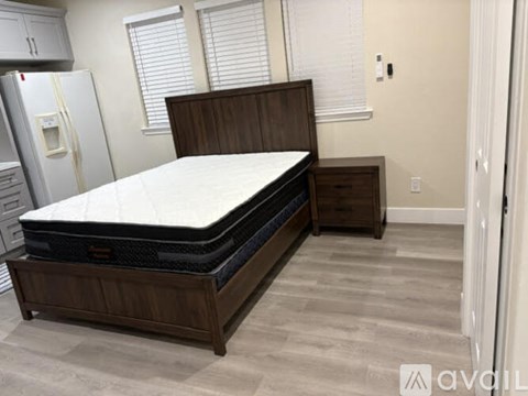 A bed with a wooden headboard and footboard is in a room with a refrigerator.