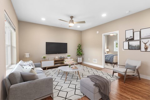 A living room with a grey couch, a coffee table, and a flat screen TV mounted on the wall.