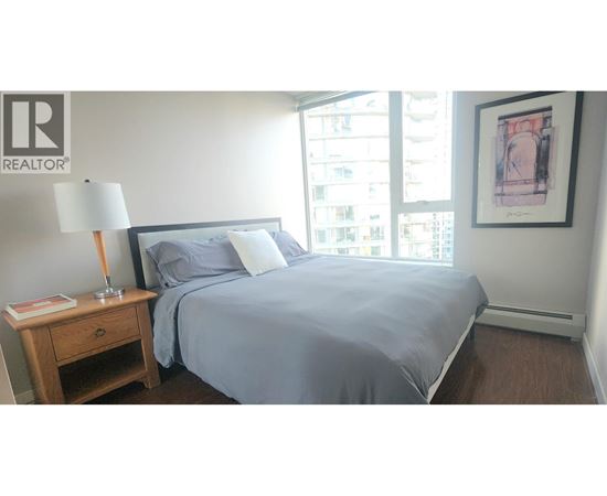 A bedroom with a bed, nightstand, and window.