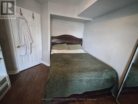 A bedroom with a bed, a coat rack, and a wooden floor.