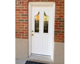 A white door with glass panels and a gold doorknob is set in a brick wall.