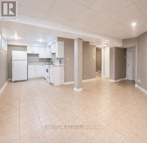 A spacious kitchen and living room with beige tiled flooring and white appliances.