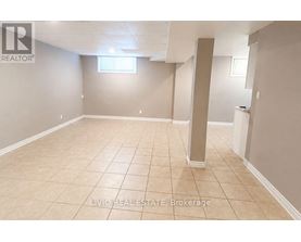 A spacious room with beige tiled flooring and white walls, with a window and a pillar in the middle.