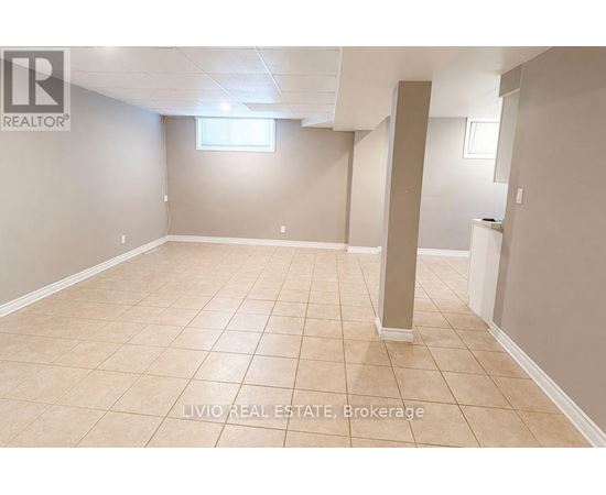 A spacious room with beige tiled flooring and white walls, with a window and a pillar in the middle.