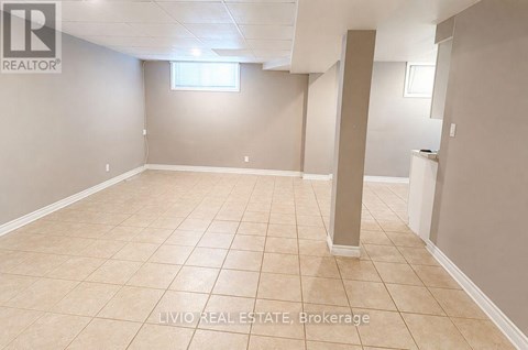 A spacious room with beige tiled flooring and white walls, with a window and a pillar in the middle.