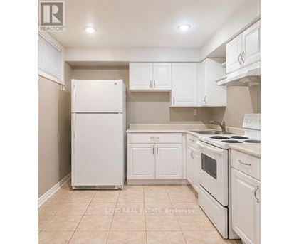 A white refrigerator stands in a kitchen with white cabinets and a white stove.