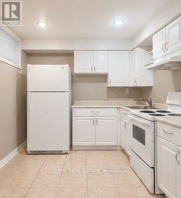 A white refrigerator stands in a kitchen with white cabinets and a white stove.
