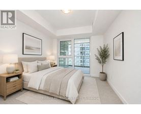 A bedroom with a large bed, a nightstand with a lamp, a potted plant, and pictures on the wall.
