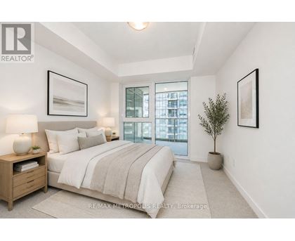 A bedroom with a large bed, a nightstand with a lamp, a potted plant, and pictures on the wall.