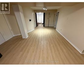 A room with wooden flooring and white walls, with a door at the end of the hallway.