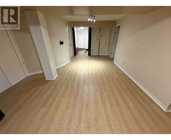 A room with wooden flooring and white walls, with a door at the end of the hallway.
