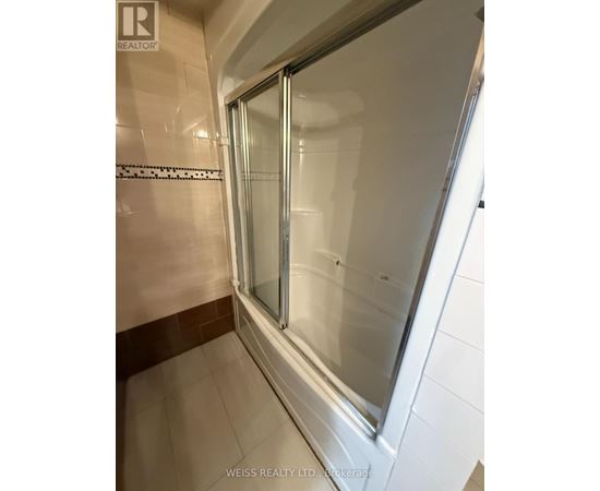 A shower area with a glass door and tiled walls.