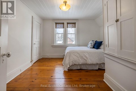 A bedroom with a bed, a window, and a wooden floor.