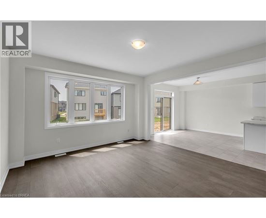 A spacious room with a large window showing a view of a house and a wooden floor.