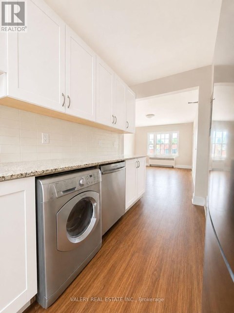 A real estate company is showcasing a modern kitchen with white cabinets and stainless steel appliances.