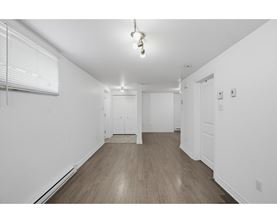 A room with white walls and wooden flooring with a window on the left.