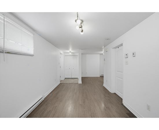 A room with white walls and wooden flooring with a window on the left.