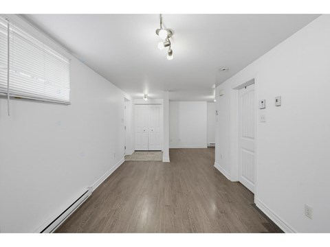 A room with white walls and wooden flooring with a window on the left.