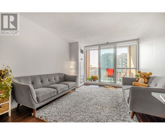 A grey sofa with a teddy bear on it in a room with a grey rug.