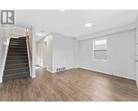 A spacious room with wooden flooring and a staircase leading to another level.