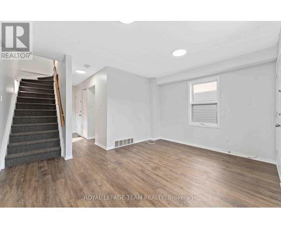 A spacious room with wooden flooring and a staircase leading to another level.