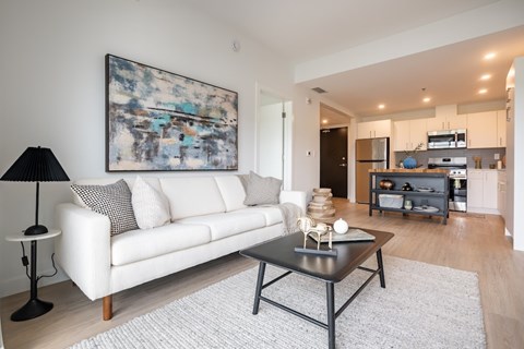 A modern living room with a white couch and a large abstract painting on the wall.