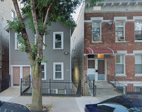 A tree in front of a grey building with a black fence.