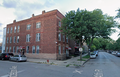 A street view of a red brick building with cars parked on the side of the road.