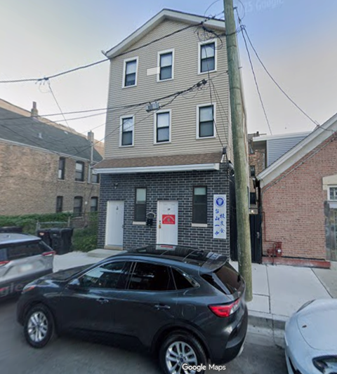 A black car is parked in front of a building with a red and white sign on the door.