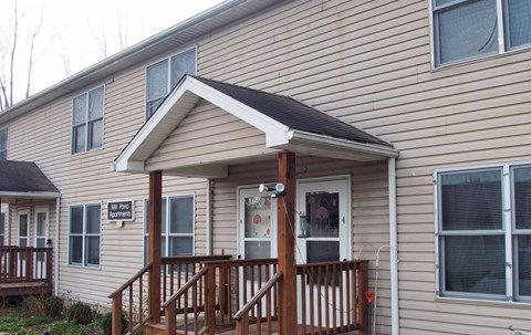 A beige house with a porch and a sign that says "Welcome to our home".