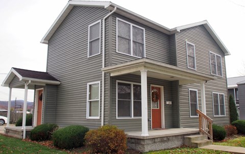 A grey house with a red door and a porch.