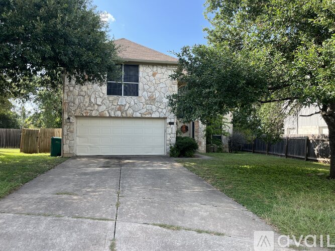 A house with a white garage door is surrounded by a fence and trees.