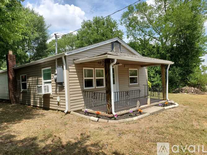 A small house with a porch is surrounded by trees.