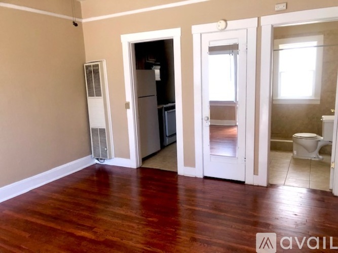 A room with a wooden floor and a white door leading to a kitchen.