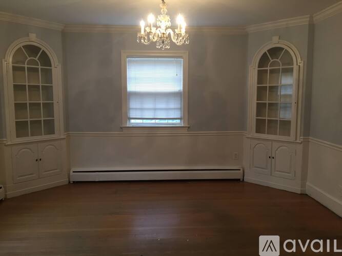A room with a chandelier, a window with blinds, and arched windows on the wall.