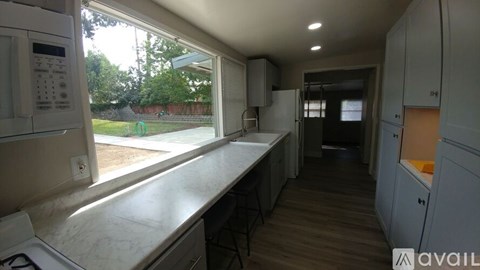 A kitchen with a white counter top and a window overlooking a yard.