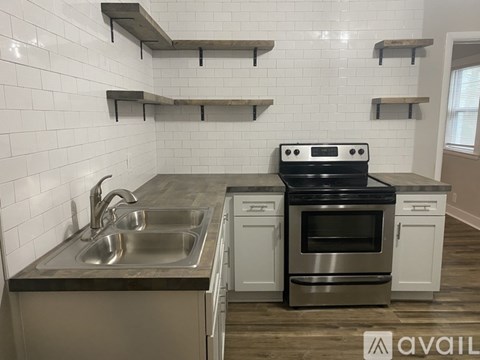 A kitchen with a stove, sink, and shelves.