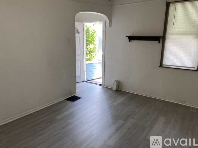 A room with a wooden floor and a white wall with a shelf and a window with blinds.
