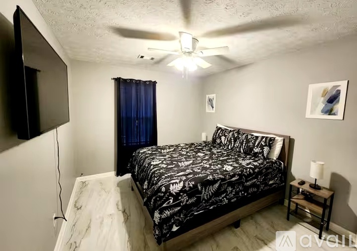 A bedroom with a bed, a ceiling fan, and a nightstand with a lamp.