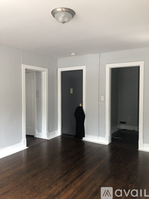 A person in a black outfit stands in the middle of a room with white walls and wooden floors.