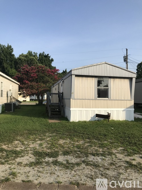 A small white building with a broken window sits in a grassy yard.