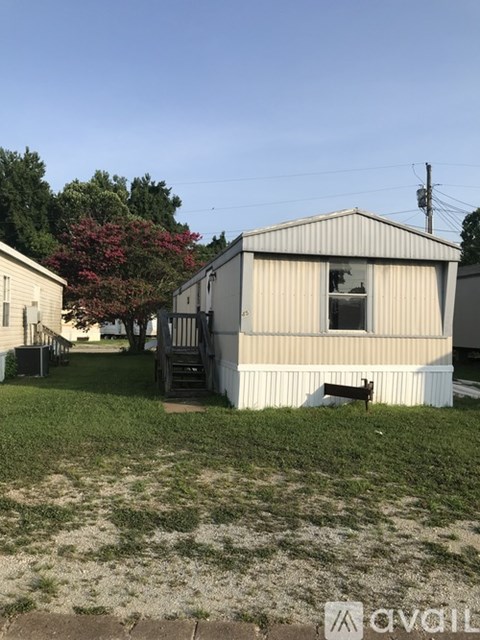 A small white building with a broken window sits in a grassy yard.